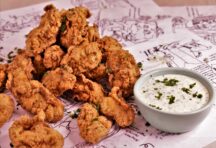 a close up of multiple peieces of crispy fried oysters next to a cup of tartar sauce