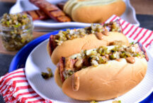 a plate of 2 grilled andouille dogs with jalapeno relish on top