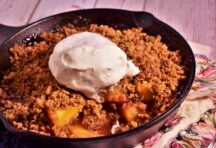 a cast iron skillet of peach crisp topped with a dallop of whipped cream