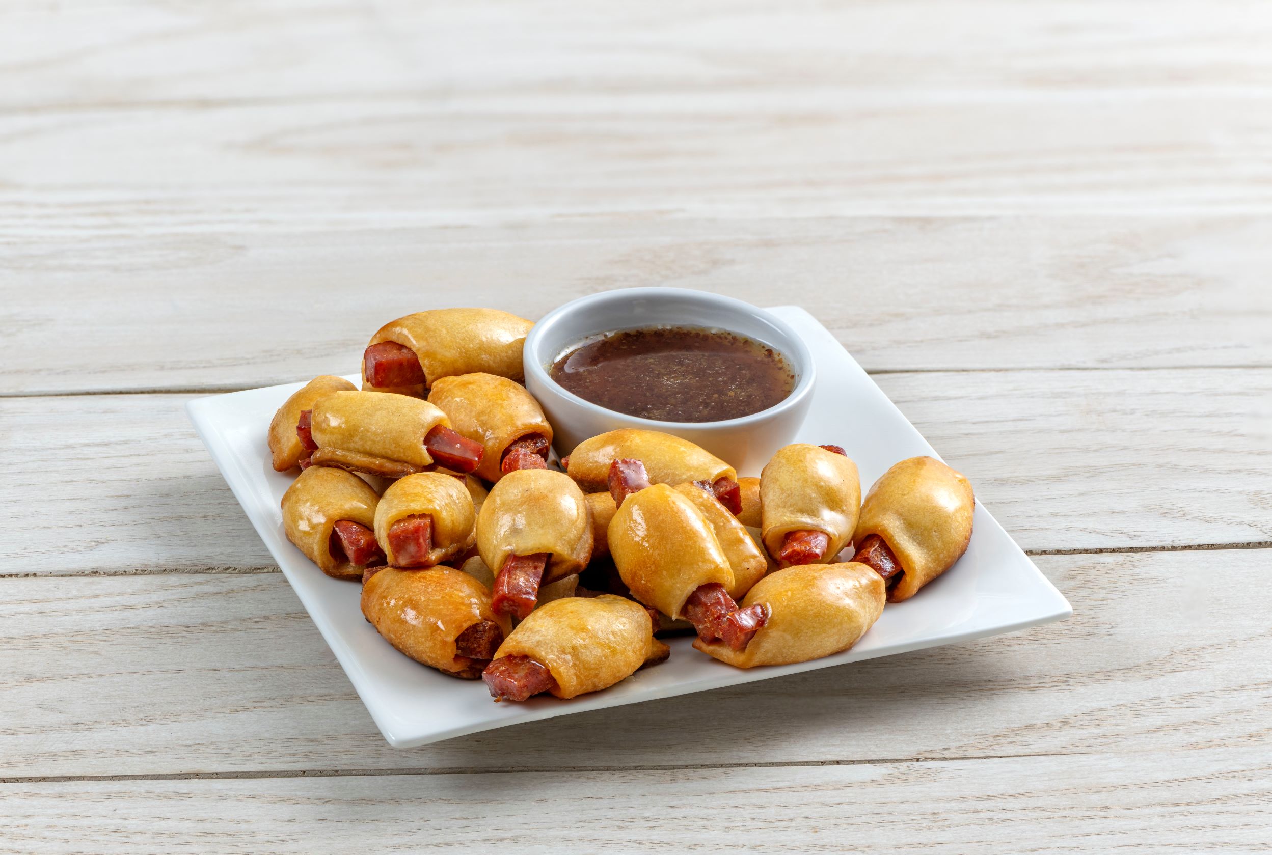 a plate of andouille puffs with a diping cup of bourbon mustard glaze