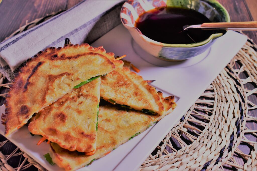 a plate of savory korean pancakes with a dipping cup full of soy pepper sauce