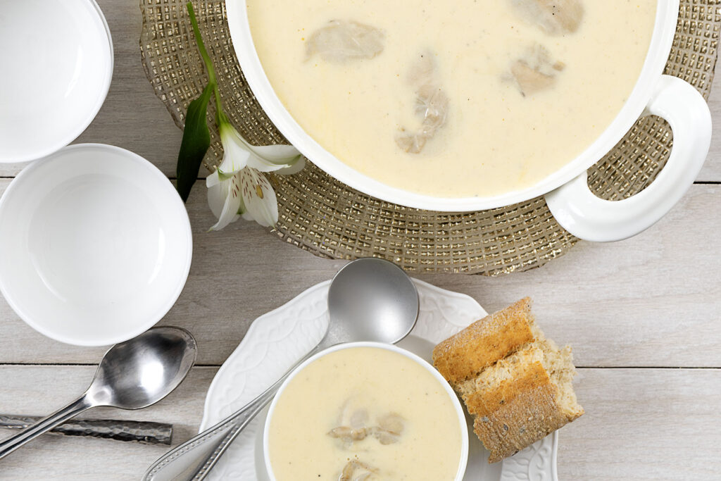 a dutch oven full of oyster and brie soup next to a bowl of the oyster and brie soup and a piece of bread