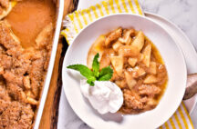 a plate of crustless apple pie with a dallop of whip cream and a green garnish next to a pan of crustless apple pie