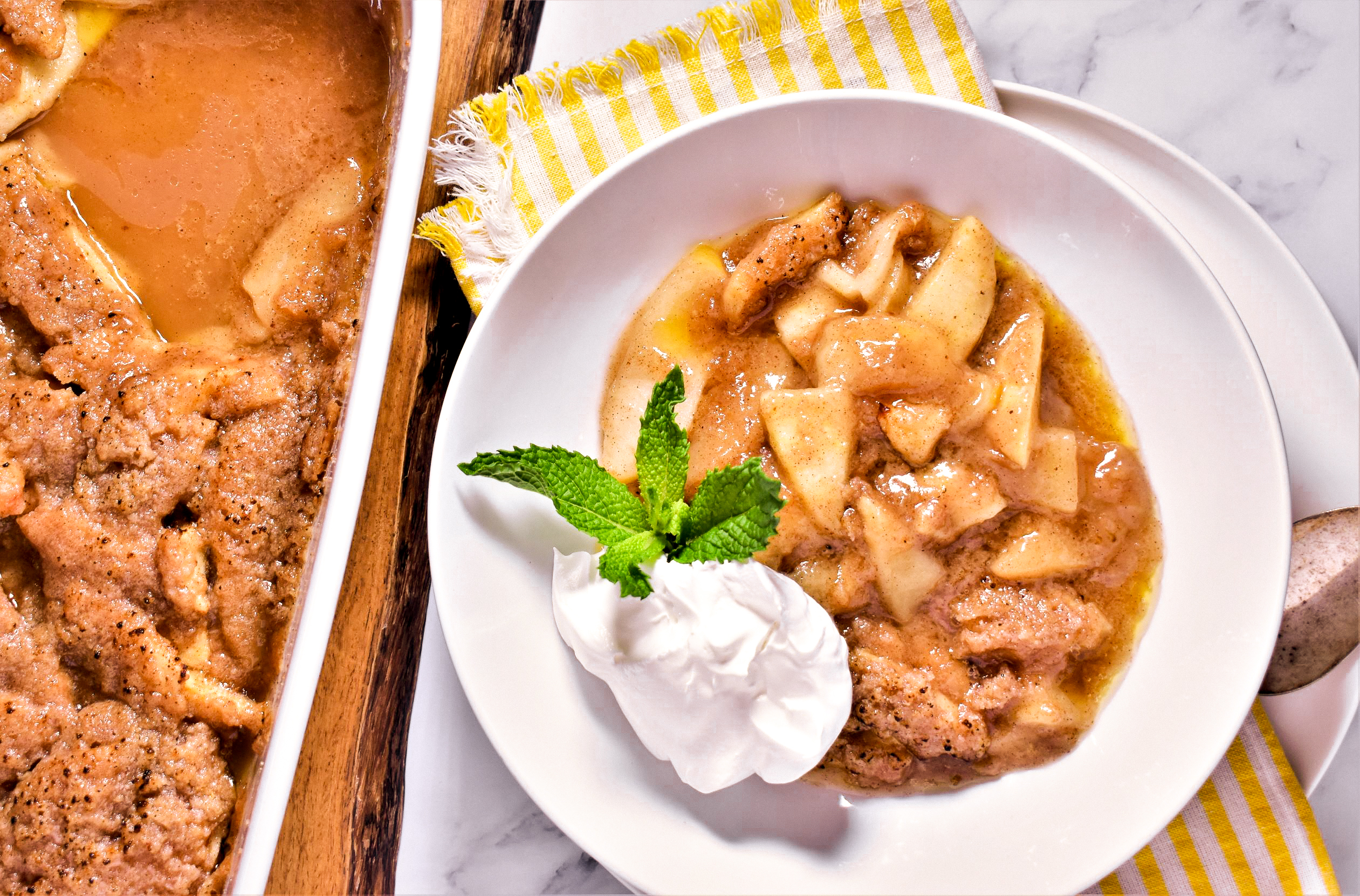 a plate of crustless apple pie with a dallop of whip cream and a green garnish next to a pan of crustless apple pie