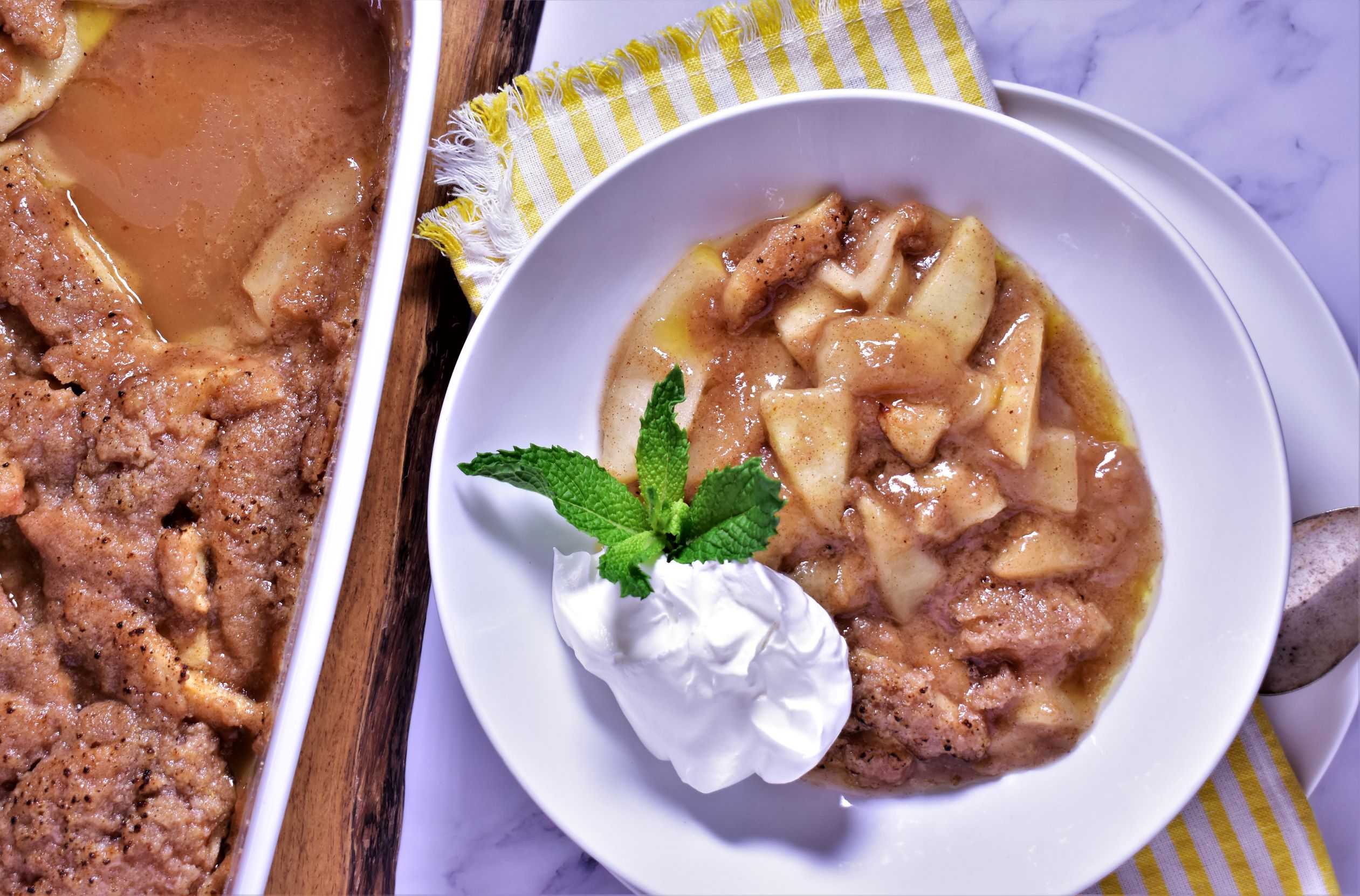 a plate of crustless apple pie with a dallop of whip cream and a green garnish next to a pan of crustless apple pie