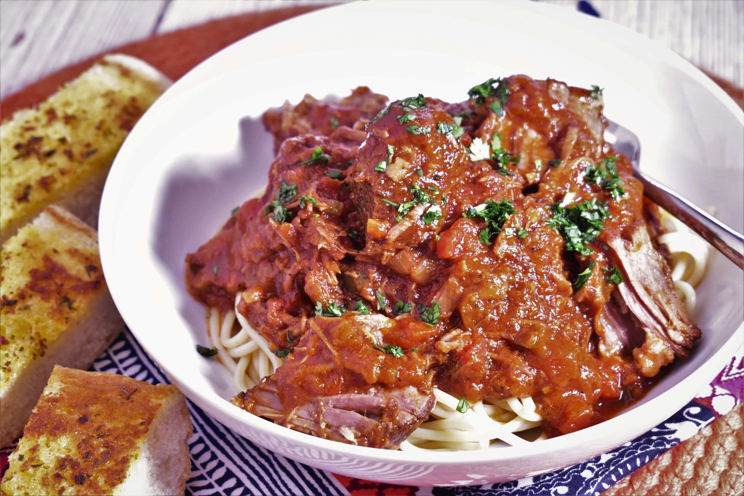 a bowl of creole daube next to a few pieces of garlic bread