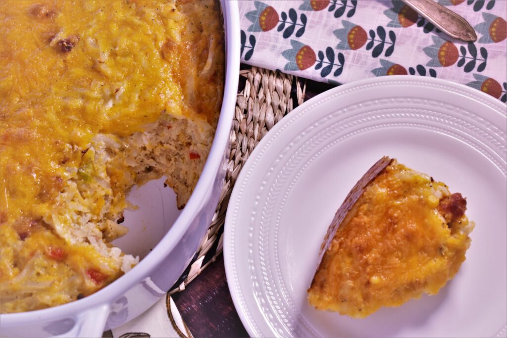 a piece of hashbrown and andouille casserole next to the bowl of hashbrown and andouille casserole