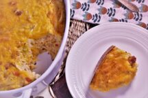 a piece of hashbrown and andouille casserole next to the bowl of hashbrown and andouille casserole