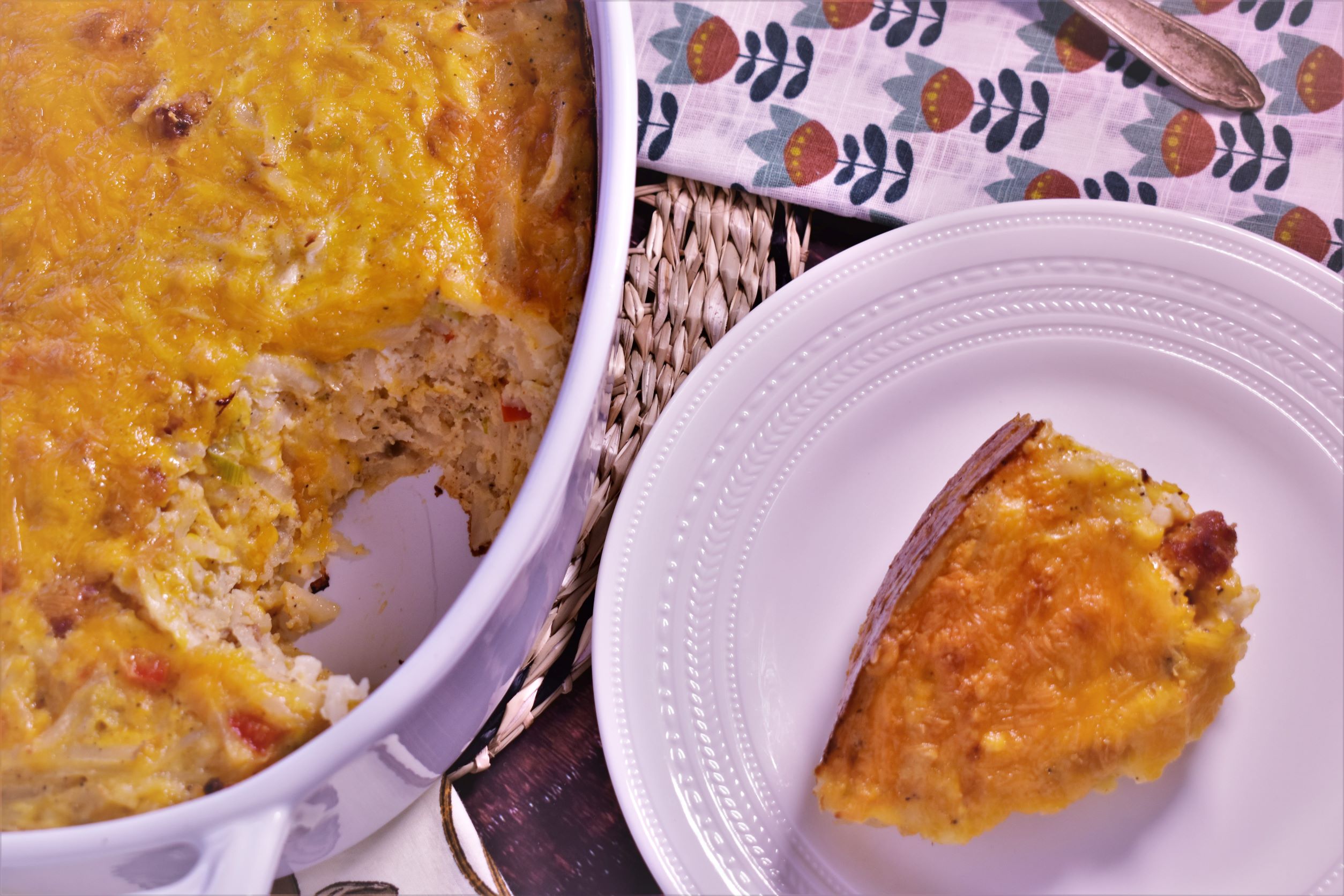 a piece of hashbrown and andouille casserole next to the bowl of hashbrown and andouille casserole