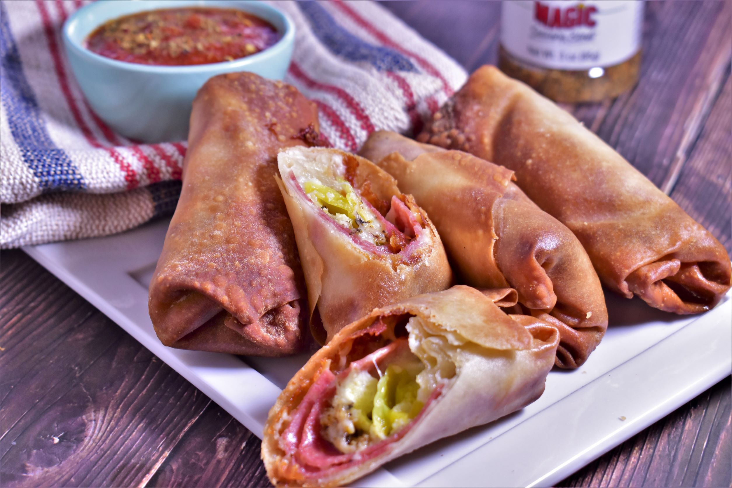 a plate of 4 air fryer italian eggrolls with one roll cut inhalf to show insides