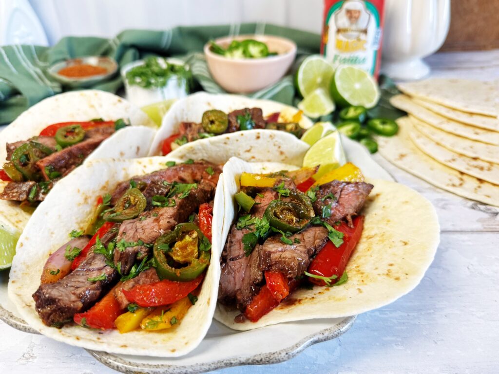 Steak fajitas in flour tortillas with grilled peppers, onions, jalapeños, and fresh cilantro, served with lime wedges and Chef Paul Prudhomme's Magic Fajita seasoning.