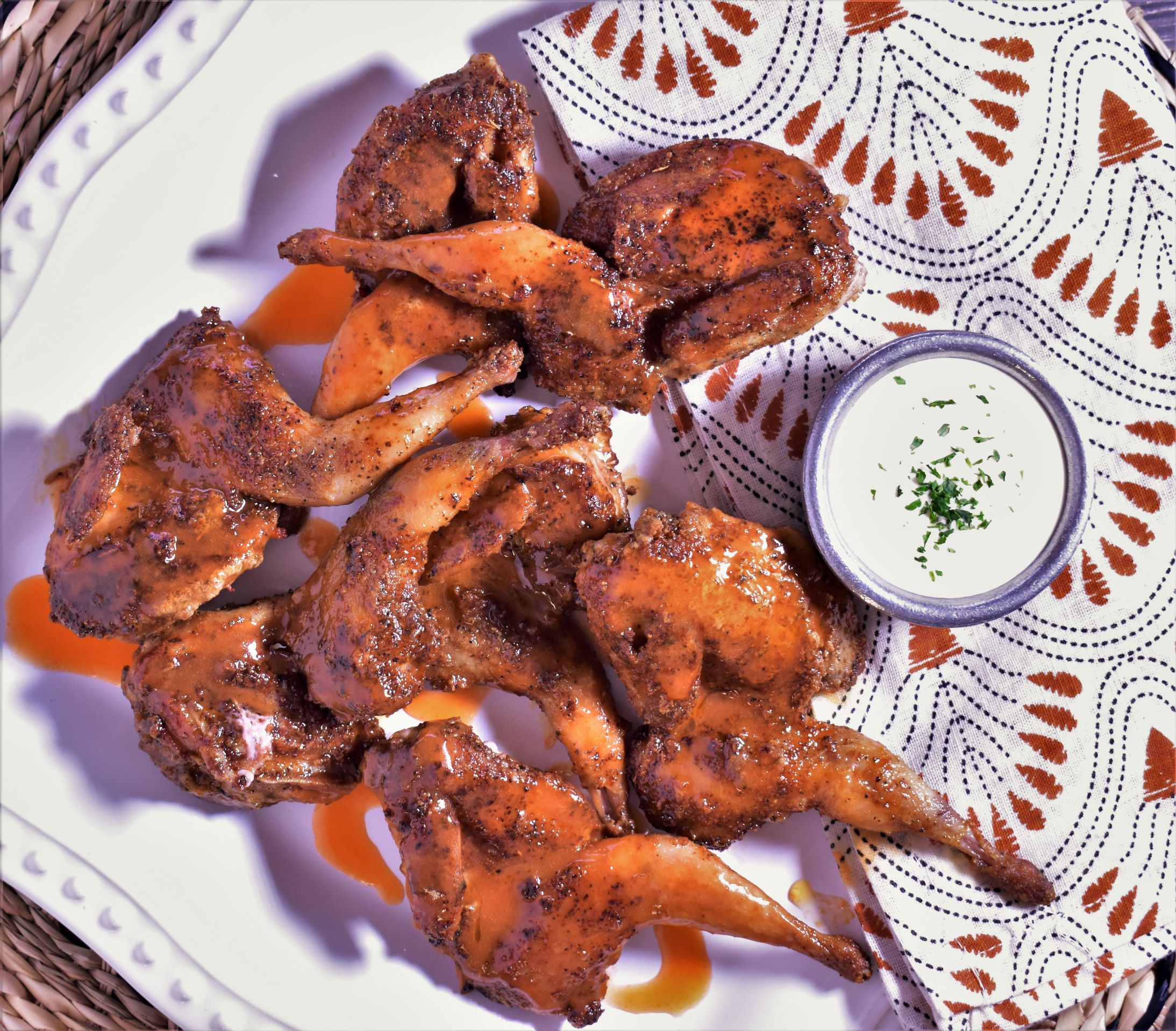 A plate of buffalo quail with a decorated napkin and a side of ranch in a cup