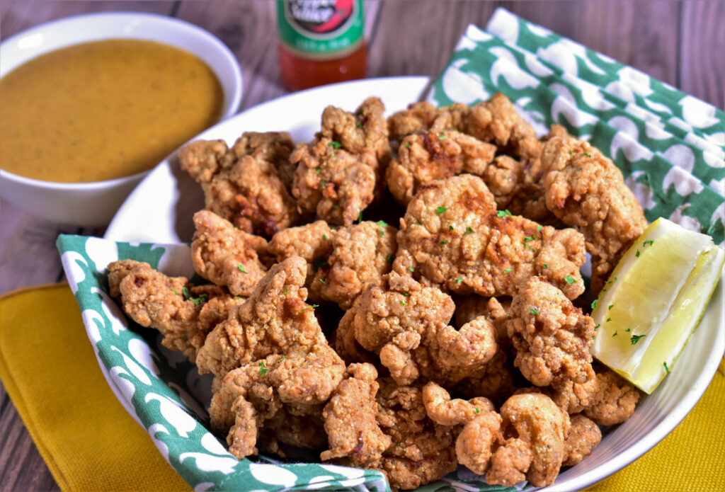 a plate full of fried alligator with a slice of lemon and dipping sauce on the side