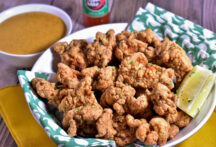 a plate full of fried alligator with a slice of lemon and dipping sauce on the side