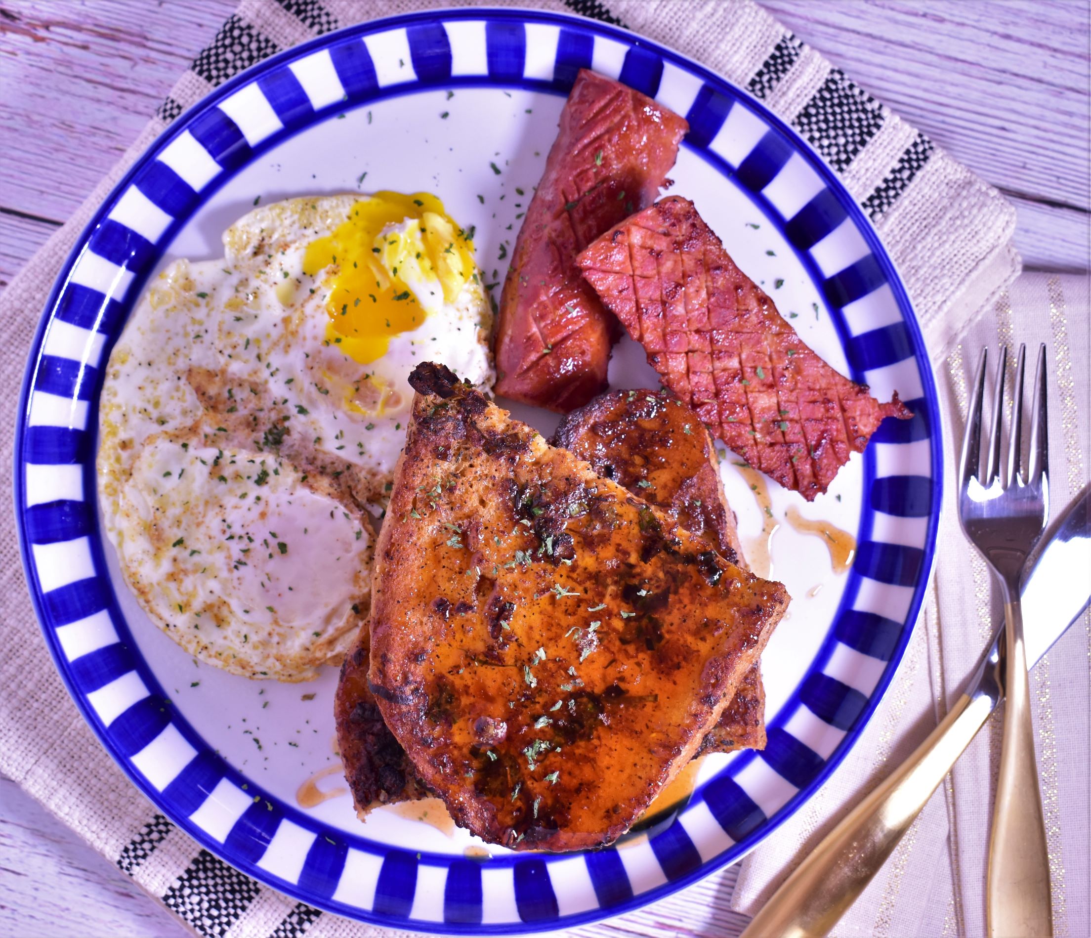 a plate of savory french toast with a side of cooked ham and fried eggs