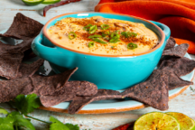 a picture of queso dip in a light blue bowl with blue corn chips and slices of lime