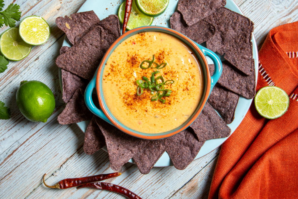 a picture of queso dip in a light blue bowl with blue corn chips and lime