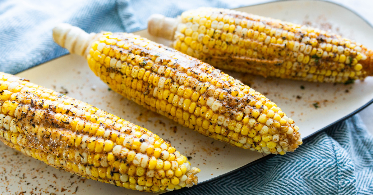 three corn on the cob on a platter on top of a blue kitchen towel