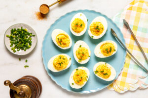 Deviled eggs topped with green onions and seasoning on a blue plate.