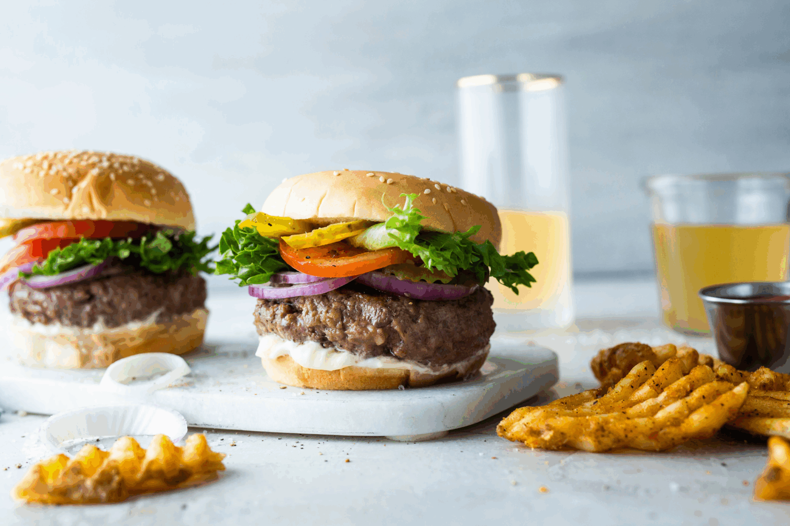 Two delicious hamburgers with fresh toppings of lettuce, tomato, onion, and cheese on a rustic cutting board.