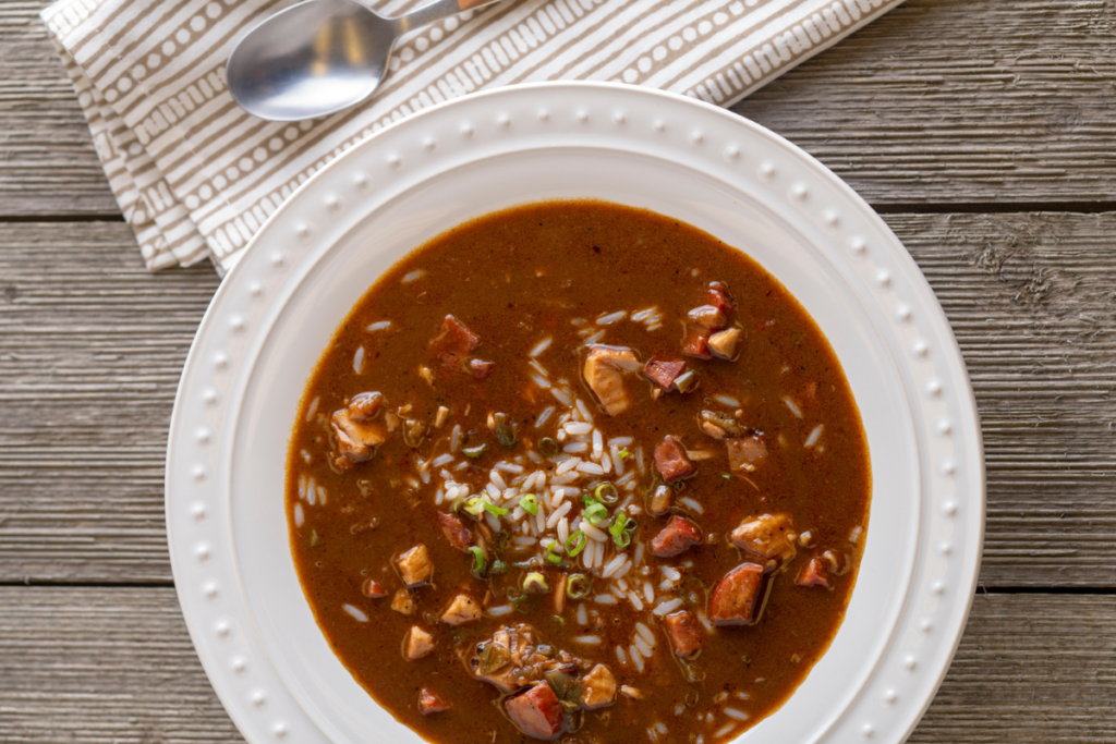 A bowl of chicken and sausage gumbo, rich in color with vegetables and spices, served with rice.
