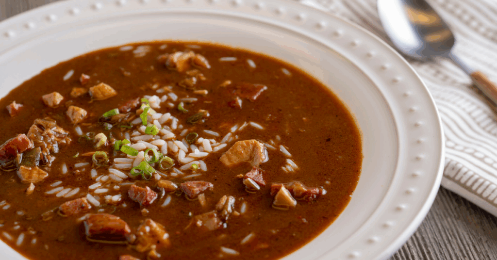 A bowl of chicken and sausage gumbo, rich in color with vegetables and spices, served steaming hot.