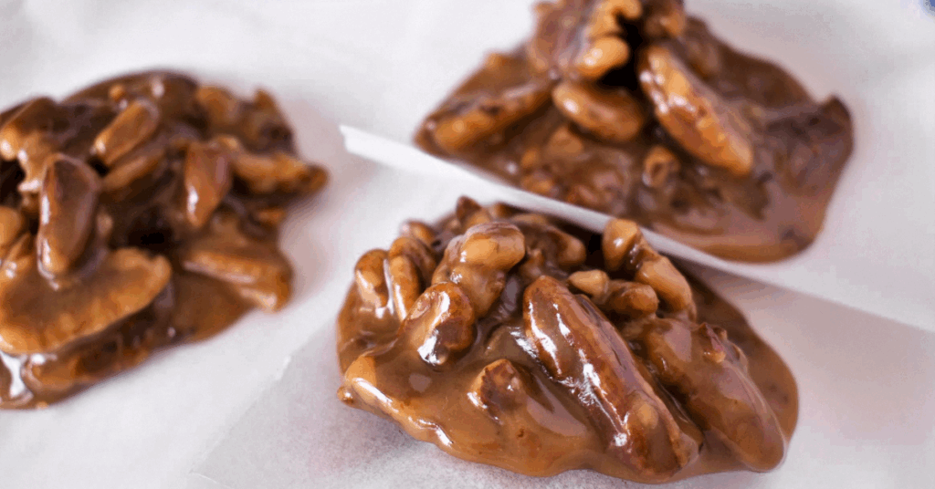 Close-up of homemade pecan pralines on parchment paper, showcasing glossy caramel and whole pecans in a clustered arrangement.