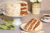 A round Spiced Pecan Cake with Pecan Frosting cake on a plate with a slice removed, revealing its layered interior and frosting.