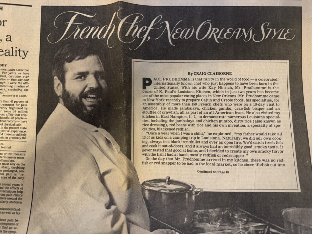 A black-and-white newspaper article titled "French Chef, New Orleans Style" features a smiling Chef Paul Prudhomme alongside a story detailing his rise to fame and the popularity of K-Paul’s Louisiana Kitchen.