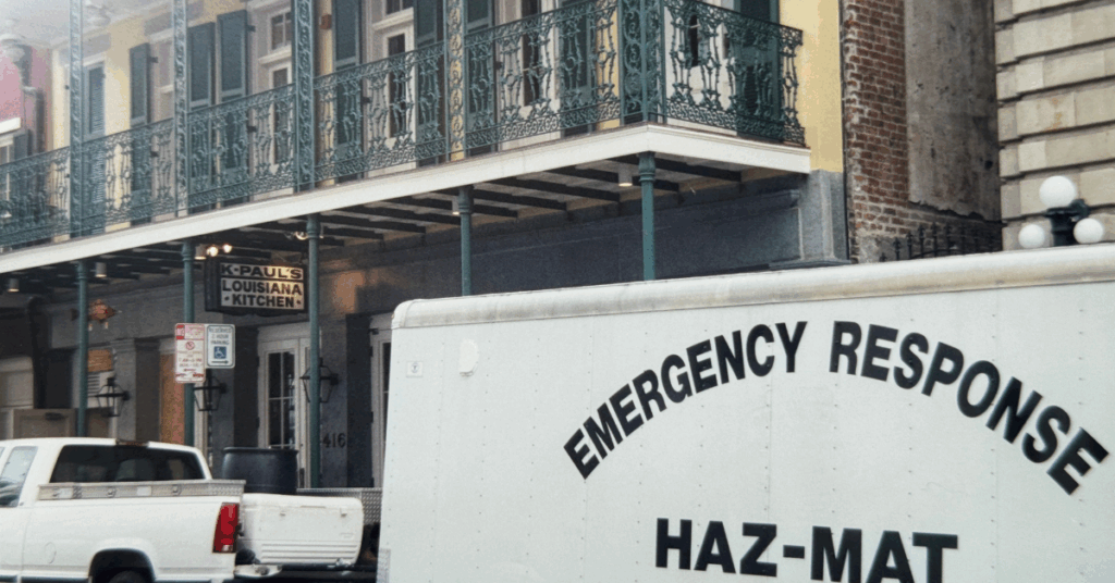 A white truck with "Emergency Response Haz-Mat" is parked outside a building featuring ornate green balconies. A sign reads "K-Paul's Louisiana Kitchen."