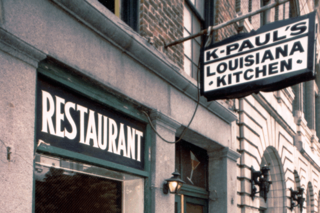 A vintage restaurant facade with a rustic sign for "K-Paul's Louisiana Kitchen" and another reading "Restaurant." The setting suggests a cozy, inviting atmosphere.