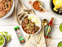 red beans in a white bowl with a bottle of magic pepper sauce and a bottle of poultry magic next to it