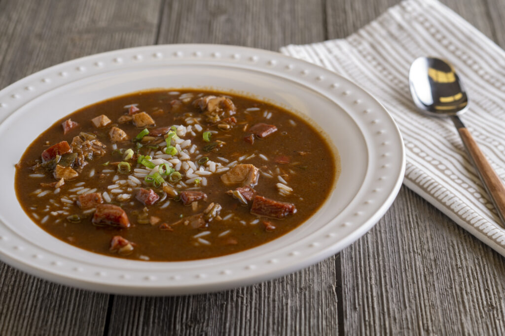 White bowl of gumbo next to a spoon, on top of a kitchen towel