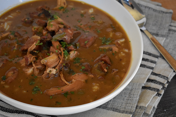 Gumbo in a white bowl on top of a kitchen towel next to a spoon