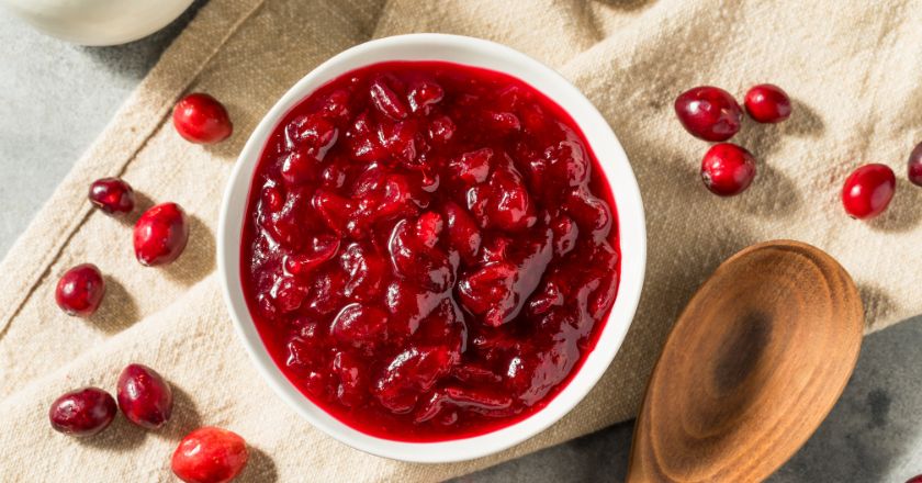 Cranberry sauce in a white bowl next to a wooden spoon, surrounded by cranberries