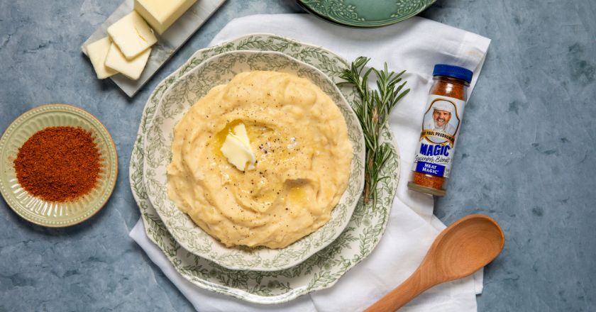 Mashed potatoes in a bowl next to a plate of spices and a wooden spoon
