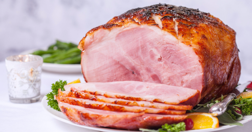 Roasted ham, sliced, on a white platter next to a cup