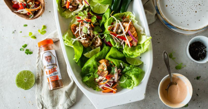 lettuce wraps on a white serving dish next to a shaker of magic seasoning