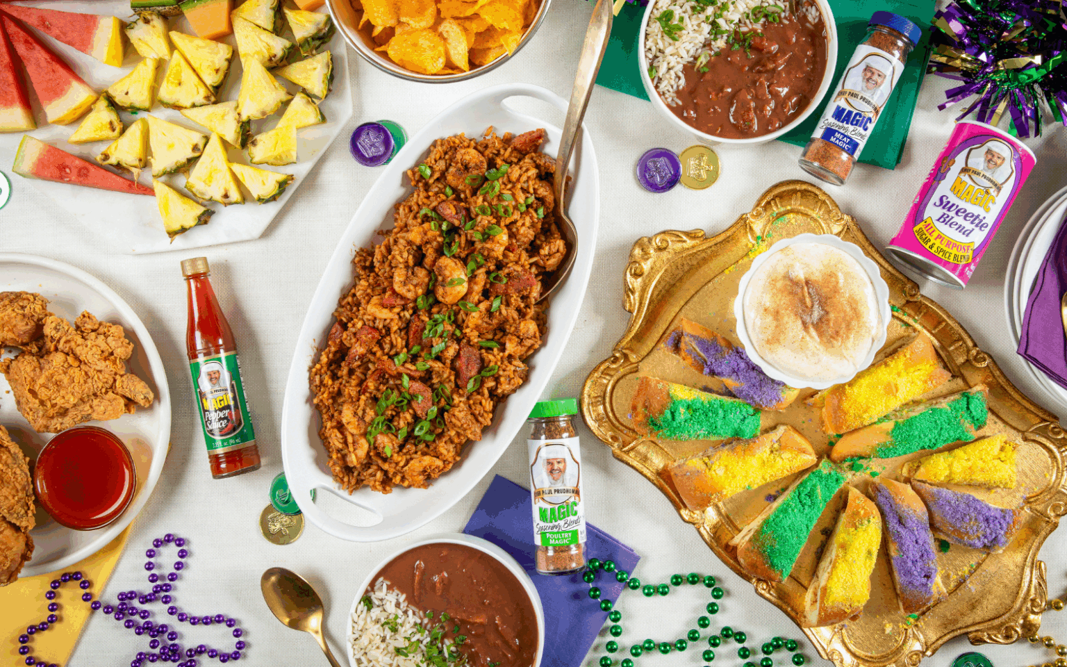 Festive table with colorful Mardi Gras decor, fried chicken, jambalaya, king cake, fruit, potato chips, hot sauce, and accessories, creating a joyful celebration.