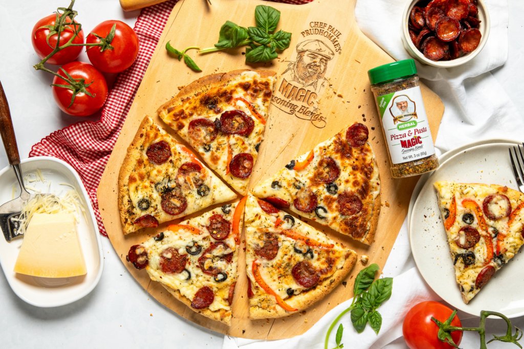 A pizza with pepperoni and olives on a wooden board, surrounded by fresh tomatoes, basil, a cheese wedge, and seasoning bottle, creating a rustic and inviting tone.