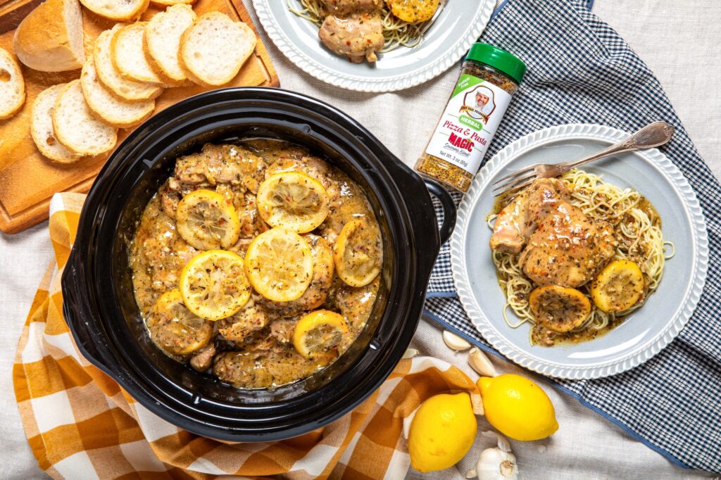 Slow Cooker Lemon Garlic Butter Chicken in a crockpot, served over pasta with Pizza & Pasta Magic seasoning.