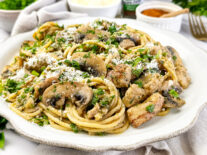 Chicken Diana pasta with fettuccine, sautéed mushrooms, and creamy sauce topped with fresh parsley and grated cheese on a white plate.